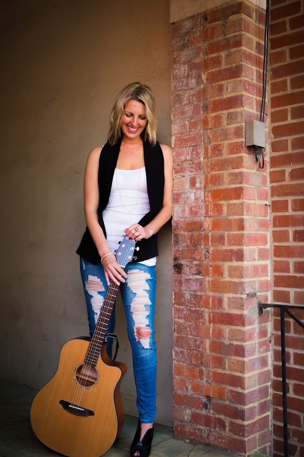Woman posing with guitar in front of brick wall